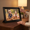 Nestory frame on a living-room sideboard, a grandmother's hand on the corner, the grandkids playing in autumn leaves on the screen