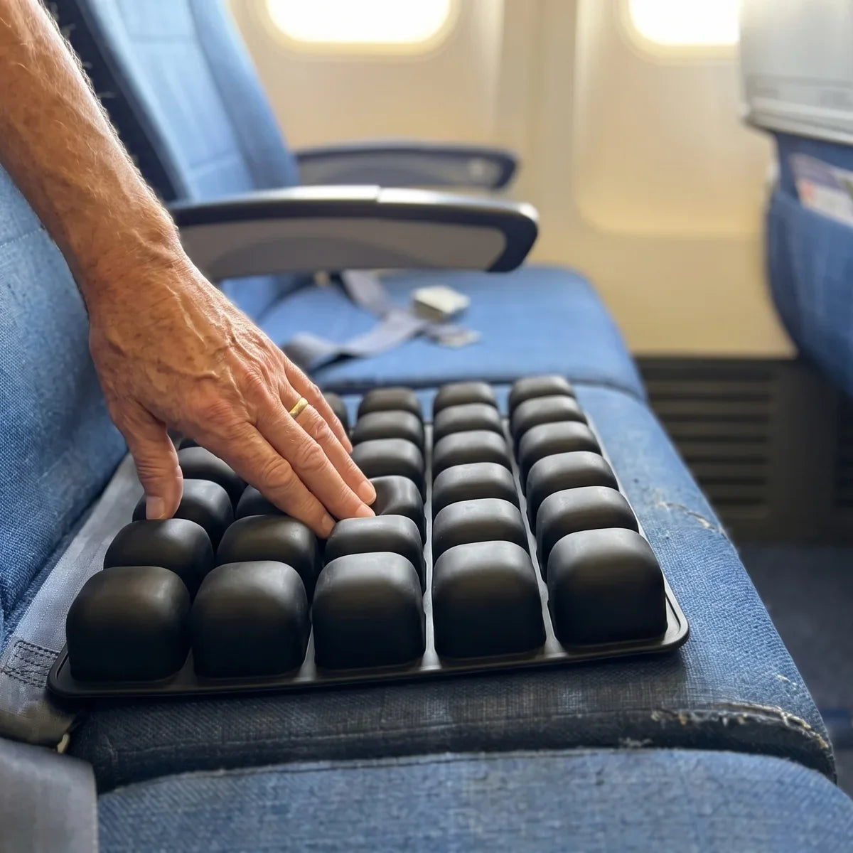 The Ralmutino air-cell cushion on an economy seat, a hand pressing one of the 36 cells