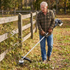 Man in safety glasses clearing weeds and brambles along a wooden fence with the steel wire head