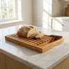 The Alba Olive Wood Bread Board with Crumb Tray in use on a kitchen island
