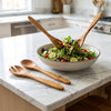 The Alba Olive Wood Serving Set (Fork + Spoon) in use on a kitchen island