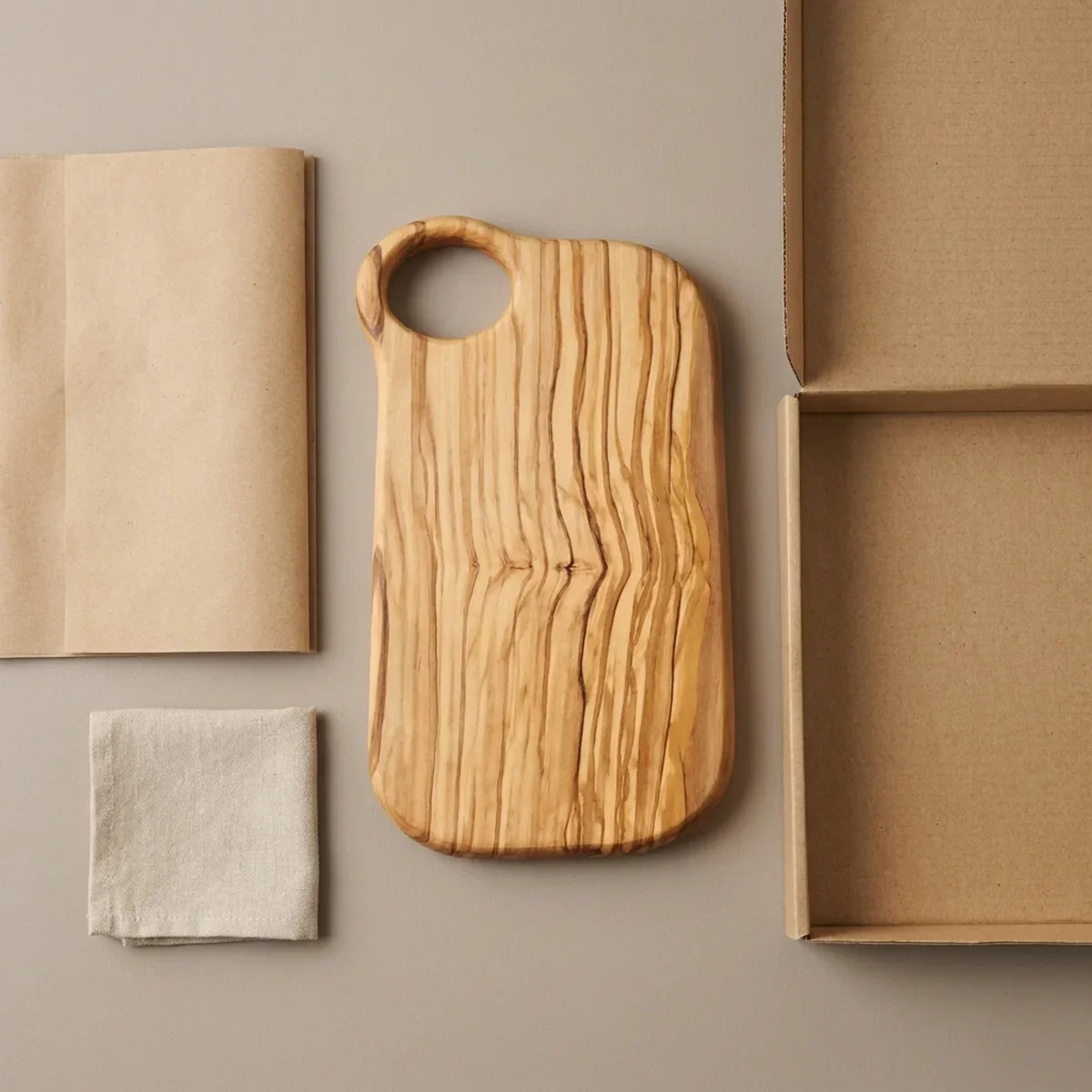 The Alba Olive Wood Board with Grip Hole with its kraft wrapping and plain shipping box